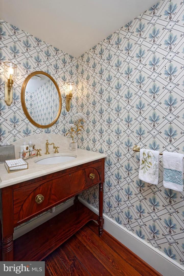 Bathroom with blue patterned wallpaper, a dark wood vanity, and an oval framed mirror.