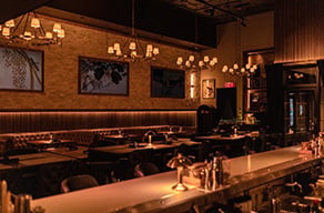 Restaurant interior with a long counter, dining tables, and warm pendant lighting.