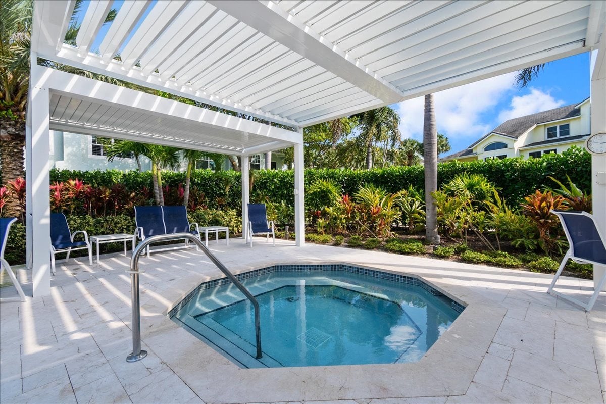 Outdoor pool beneath a white pergola, with blue lounge chairs and tropical landscaping.