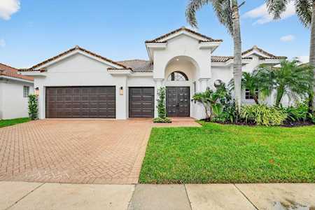 White stucco home with an arched entry, dark garage doors, brick driveway, and lawn.