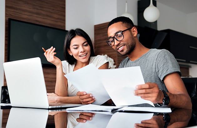 A couple reviews documents together at a kitchen island beside a laptop.