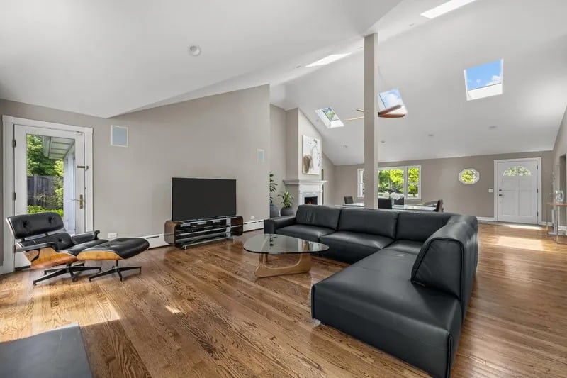 Living room with a black sectional sofa, vaulted ceiling, skylights, and hardwood floors.
