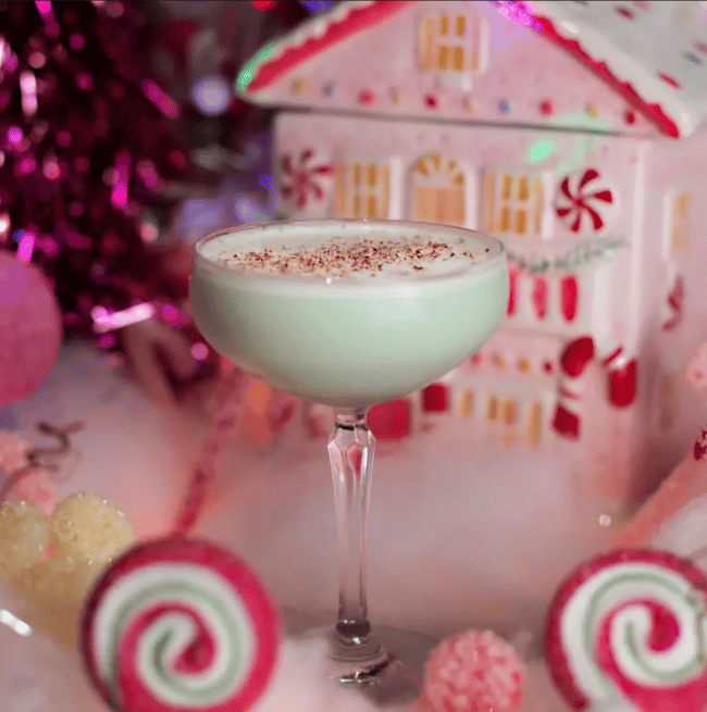 Creamy, spice-dusted cocktail surrounded by gingerbread-house and peppermint decorations.