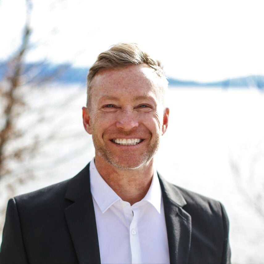 Smiling man in a black blazer and white shirt outdoors.