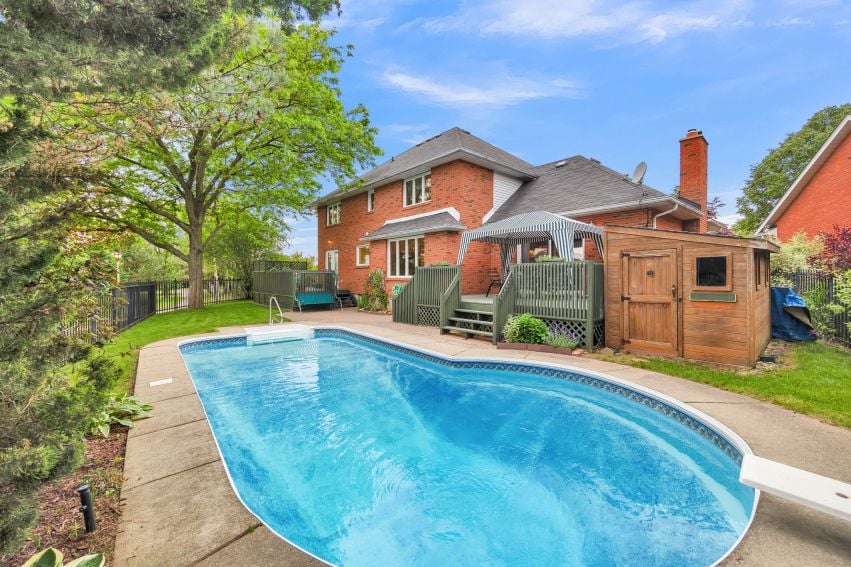 Backyard pool beside a two-story red-brick house, with a wooden deck and shed.