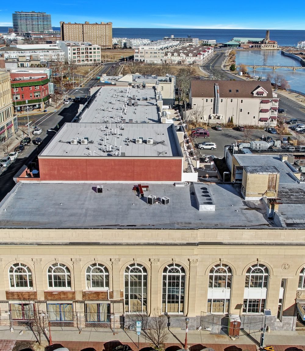 Aerial view of a historic building with arched windows, rooftops, and the ocean beyond.