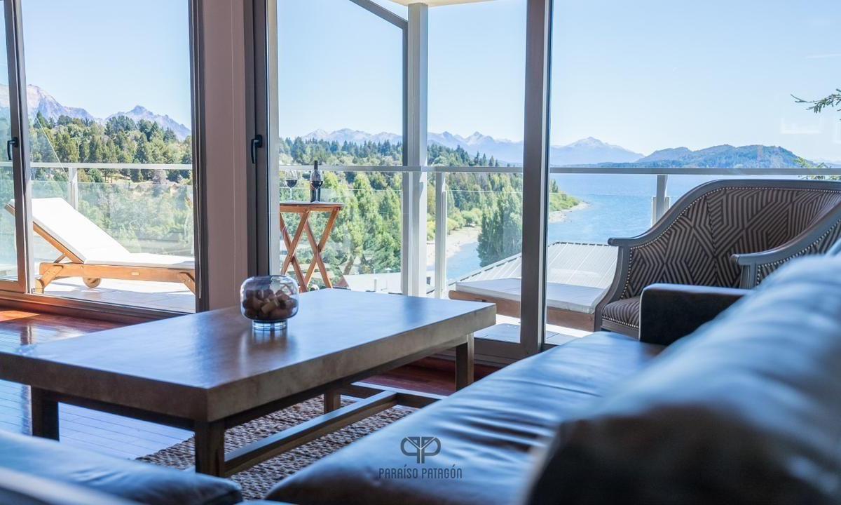Apartment living room with floor-to-ceiling windows overlooking a lake, forest, and distant mountains.