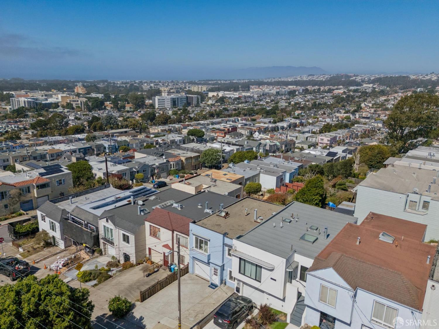 Aerial view over neighborhood rooftops toward the city and distant hills.