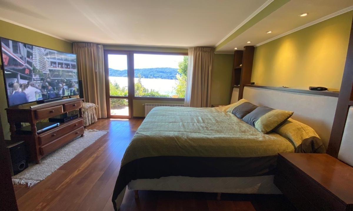 Bedroom with a large bed and glass doors overlooking a lake and wooded hills.