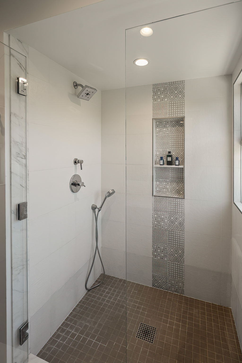 Walk-in shower with a patterned tile niche, glass enclosure, and handheld showerhead.
