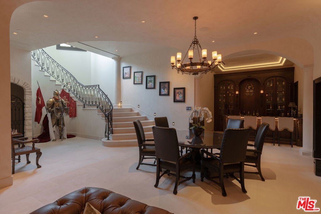 Dining area with a chandelier, ornate curved staircase, and dark wood display cabinet.