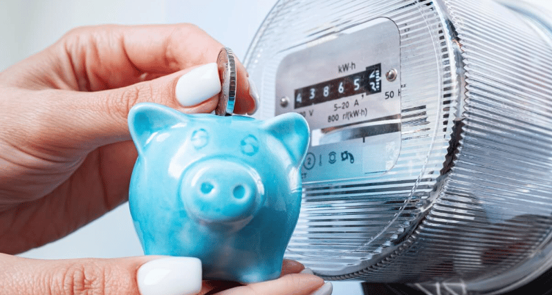A coin held over a turquoise piggy bank beside an electric meter.