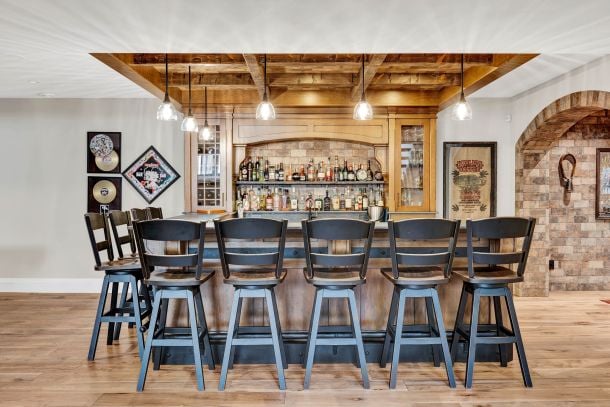 Home bar with six stools, bottle display shelves, exposed timber ceiling beams, and pendant lights.