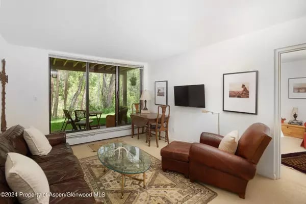 Living room with brown leather seating and large sliding glass doors overlooking trees.