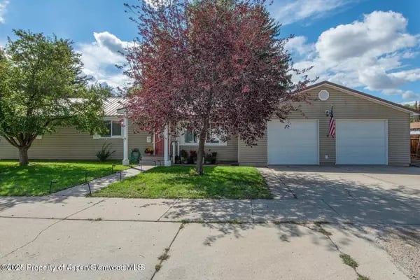 Single-story ranch home with an attached two-car garage, shaded front lawn, and American flag.