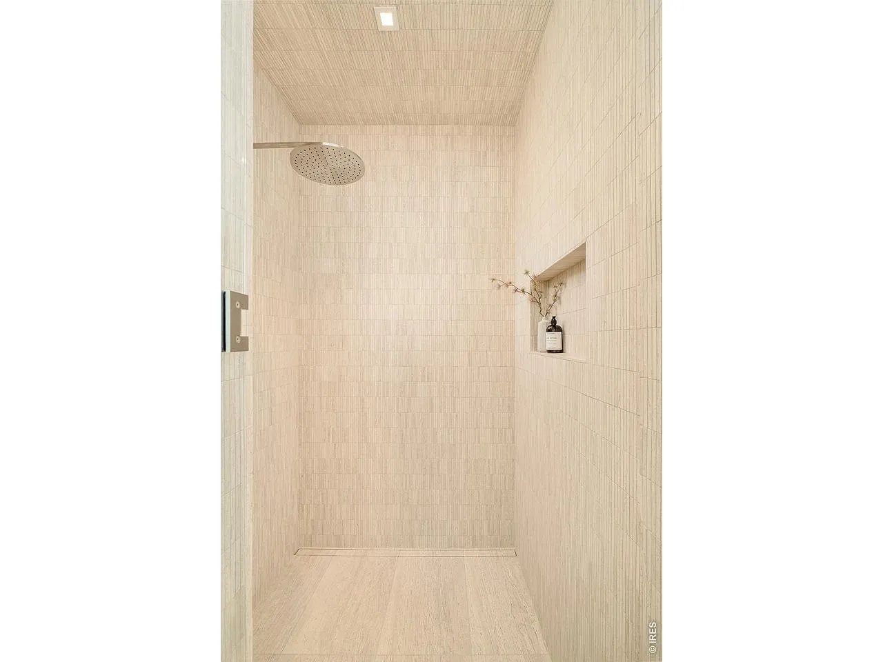 Walk-in shower with pale tiled walls, a rainfall showerhead, recessed niche, and linear drain.