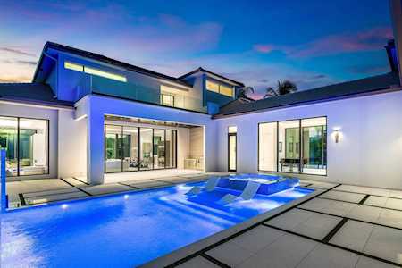 Modern home with a bright blue pool, broad patio, and illuminated glass doors at dusk.