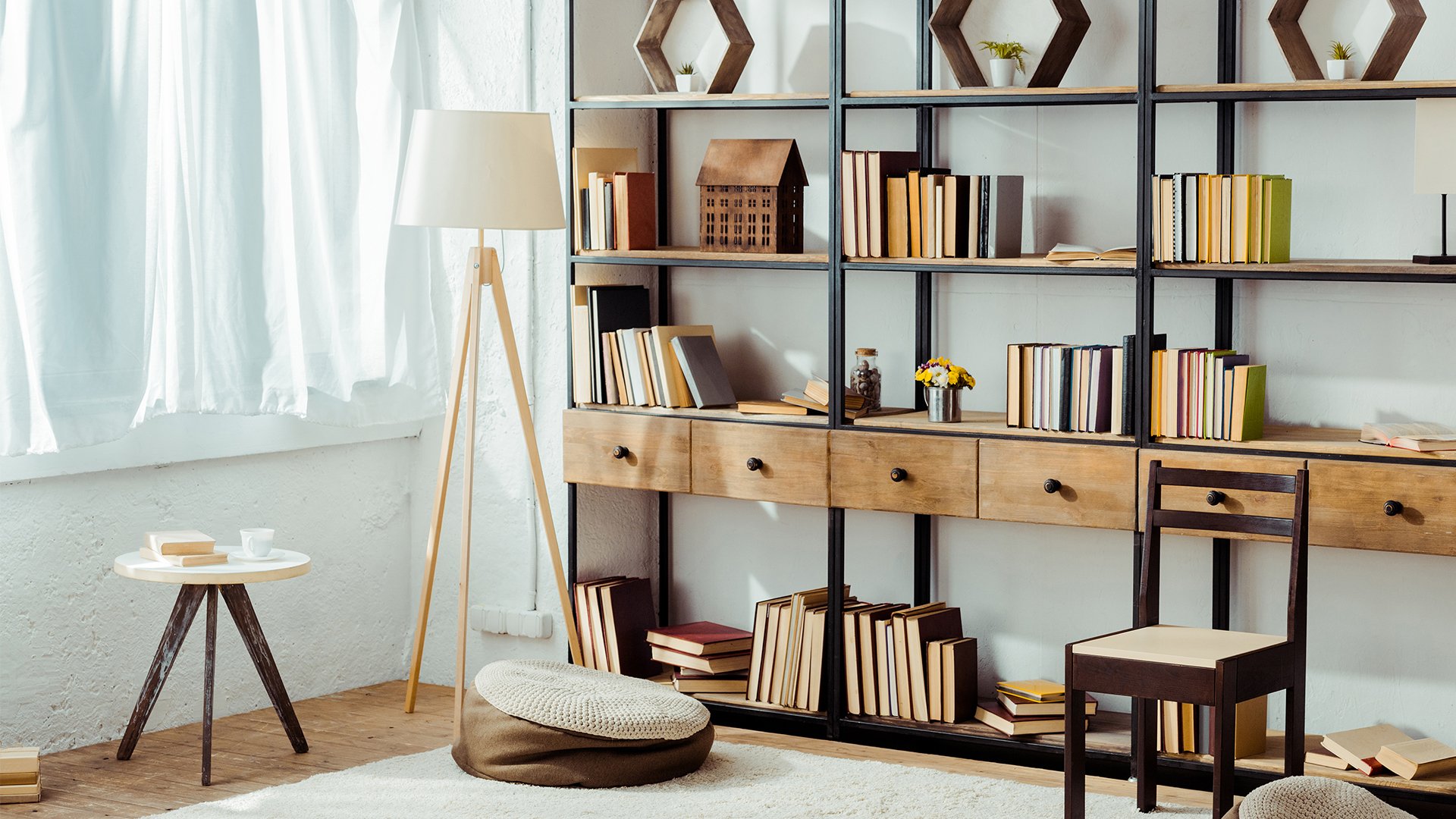 Bright home library with bookshelves, a tripod floor lamp, and a cozy reading area by sheer curtains.