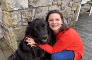 Margaret Holder crouching beside a black dog against a stone wall.