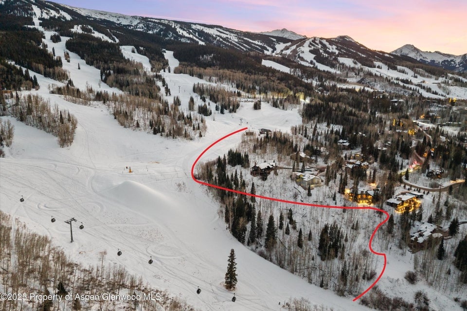 Aerial view of a snow-covered ski slope and mountain homes, with a red route line.
