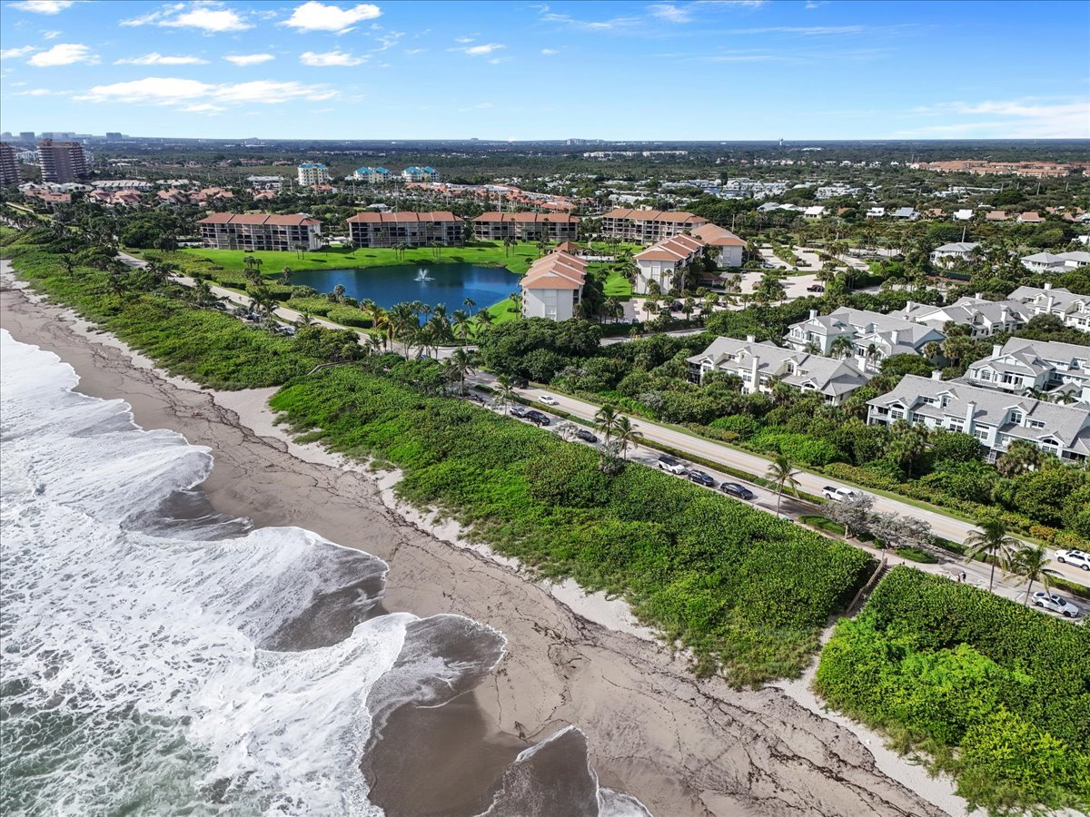 Aerial view of Sea Colony condominiums beside the beach, with a landscaped pond and coastal road.