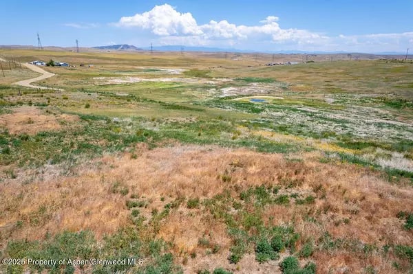 Aerial view of open grassland with a small pond, dirt road, and low hills.