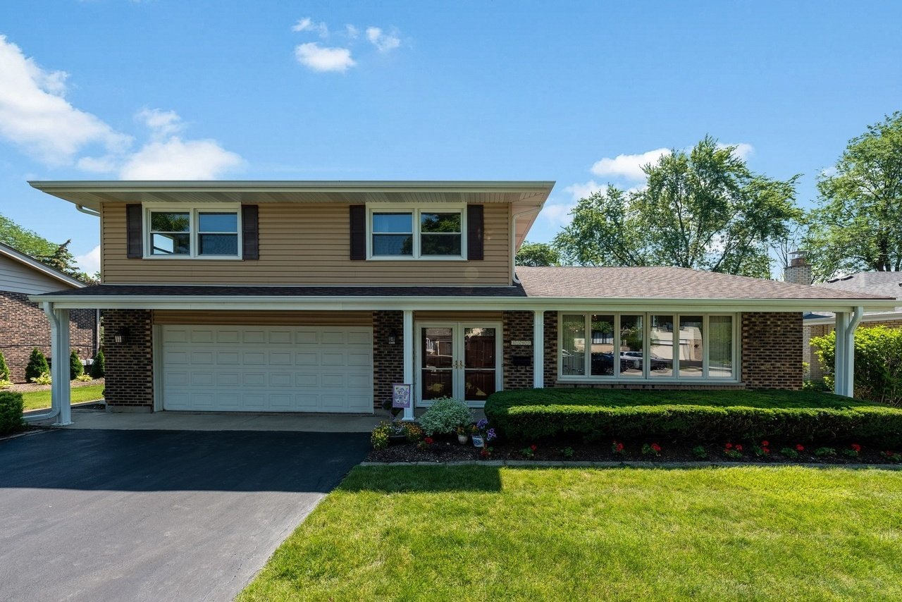 Two-story suburban home with tan siding, brick lower level, attached garage, and landscaped front lawn.