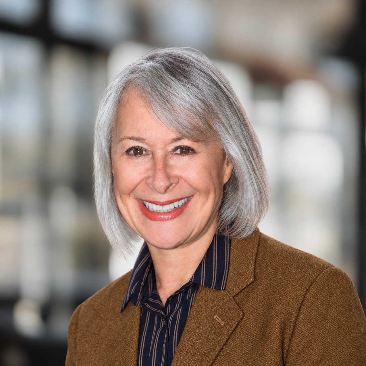 Ellen Kapit smiling in a brown blazer, with shoulder-length silver hair.