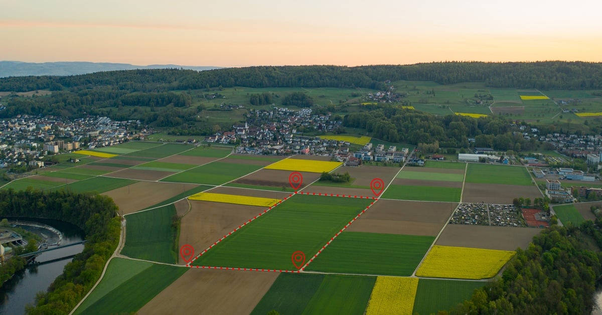 An aerial view of large plots of land in a town with one rectangular green plot highlighted with red markings.