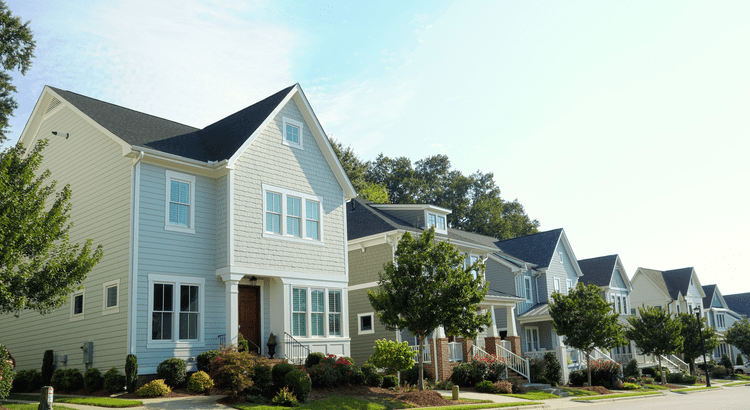 A row of two-story homes with peaked roofs, front porches, and landscaped yards.