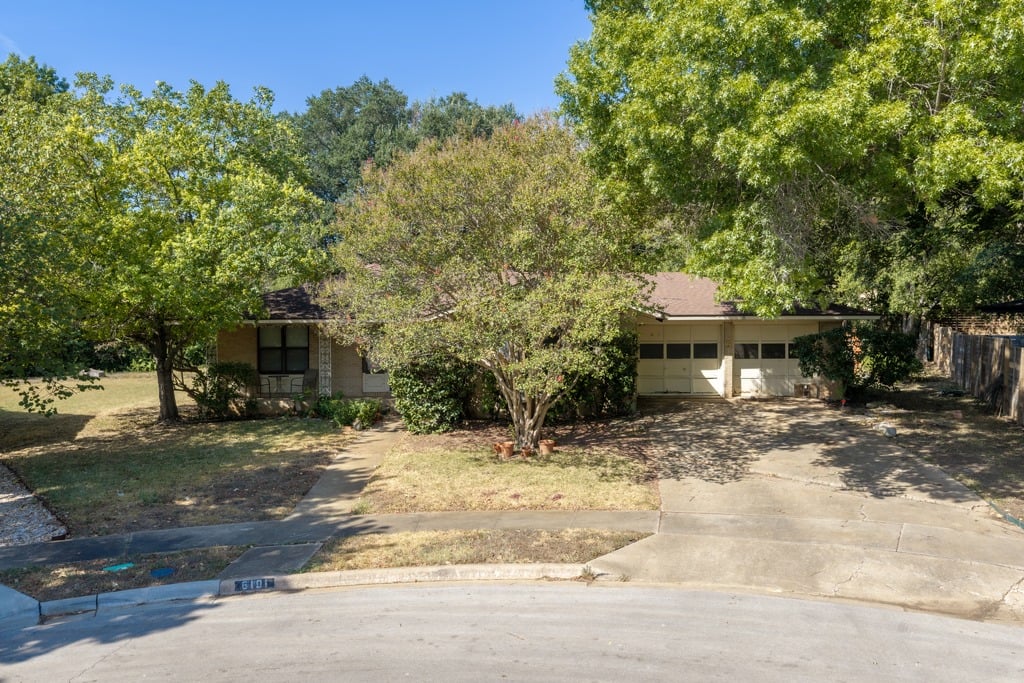 Single-story house with a two-car garage, shaded by mature trees beside a wide concrete driveway.