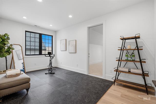 Home fitness room with a stationary bike, dark flooring, and a large black-framed window.