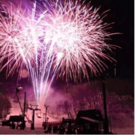 Pink and white fireworks burst over a snow-covered outdoor area at night.