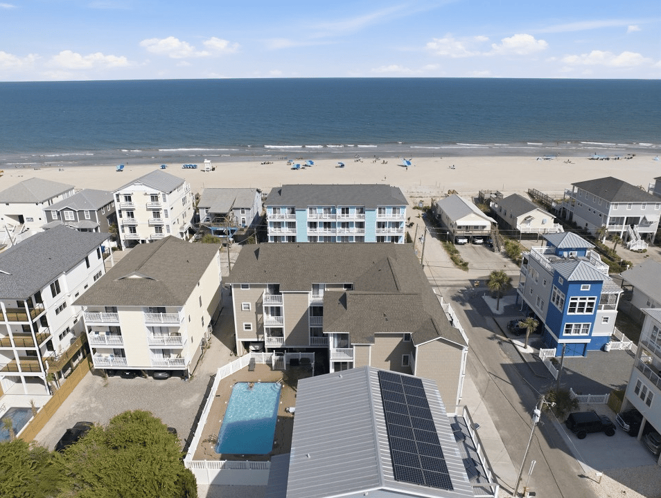 Beachfront condominium buildings beside a pool, with Carolina Beach and the ocean in the background.
