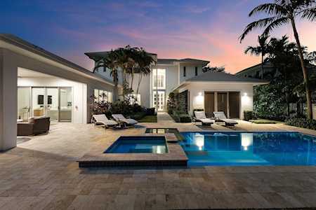 Modern home with an illuminated swimming pool, tiled patio, and palm trees at dusk.