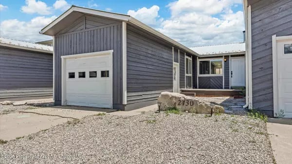 Gray-sided home with garage doors and a gravel driveway; stone address marker reads 2430.