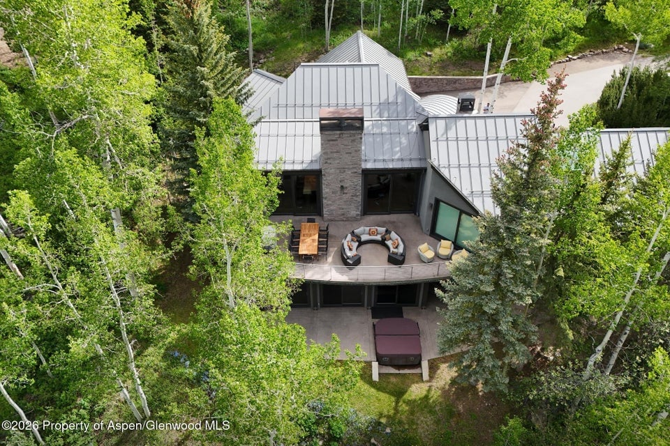 Aerial view of a modern mountain home with a furnished deck, surrounded by dense green trees.