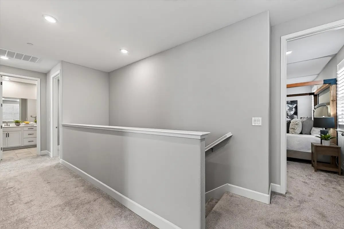 Carpeted upstairs hallway and stair landing, with a bedroom and bathroom visible through open doorways.