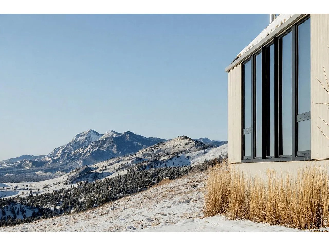 Modern home beside snow-covered foothills and distant mountain peaks.