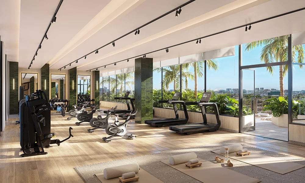 Bright fitness room with cardio equipment, yoga mats, and palm-lined city views.