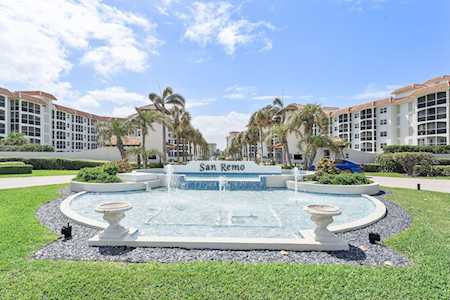 San Remo condominium buildings behind a landscaped entrance fountain and palm-lined drive.