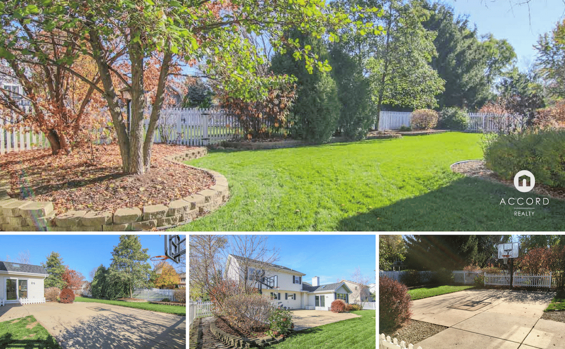 Colonial home and fenced backyard with a broad lawn, landscaped garden, paved driveway, and basketball hoop.