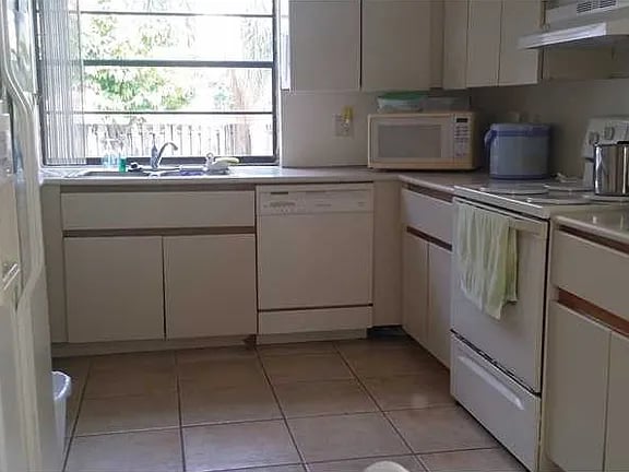 Compact kitchen with white cabinets, tiled floor, and a sink beneath a large window.