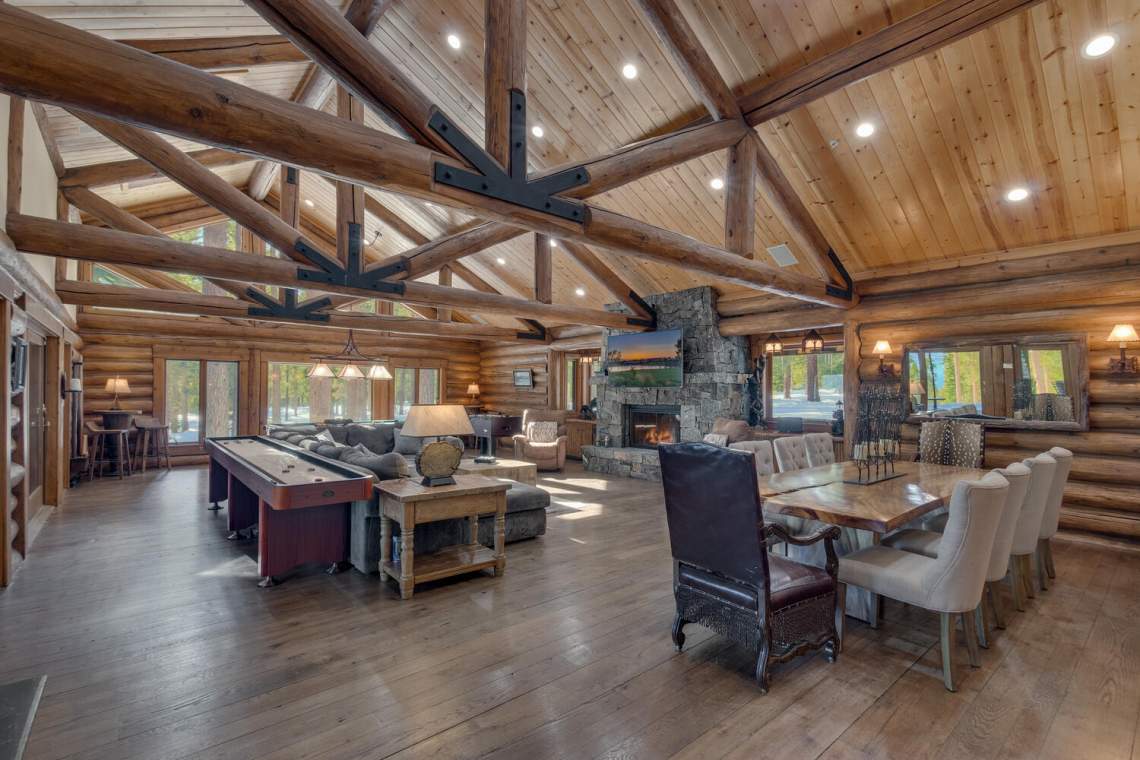 Great room with exposed timber trusses, a stone fireplace, pool table, and dining area.