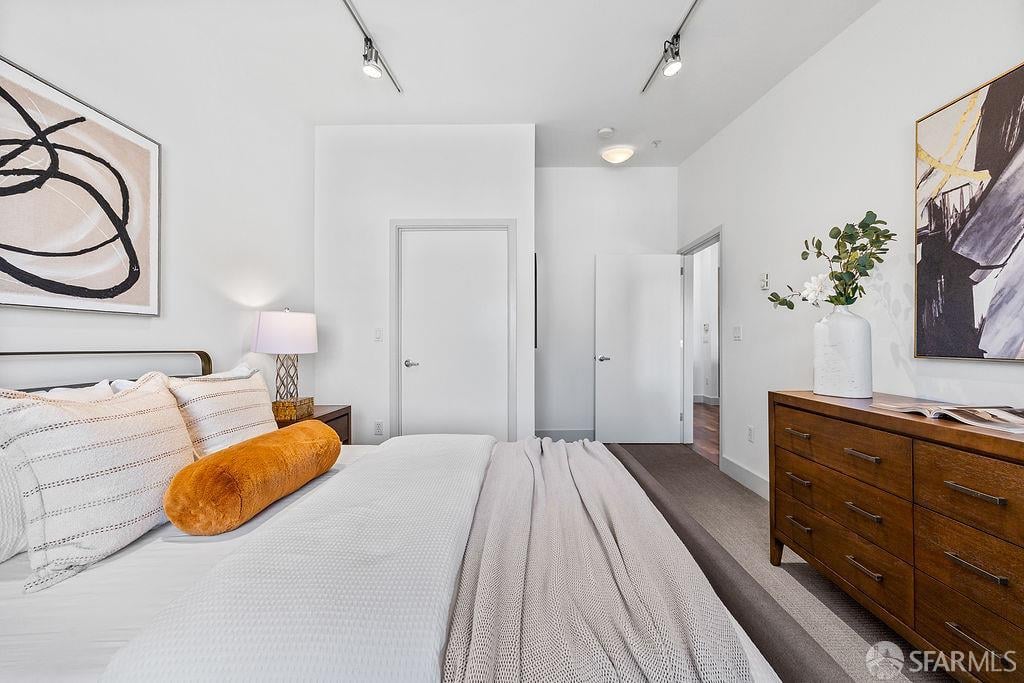 Furnished bedroom with a white bed, orange bolster pillow, abstract art, and wooden dresser.