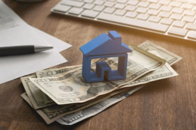 a-blue-home-figurine-resting-on-a-money-with-a-contract-in-the-background