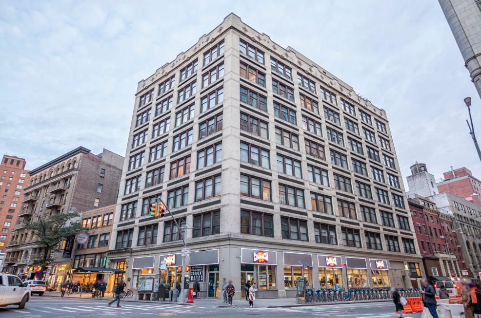 The Peterfield’s light stone corner facade rises above street-level shops and a busy city intersection.