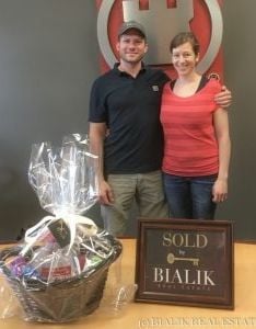 A couple celebrates their closing beside a gift basket and a SOLD BY BIALIK plaque.