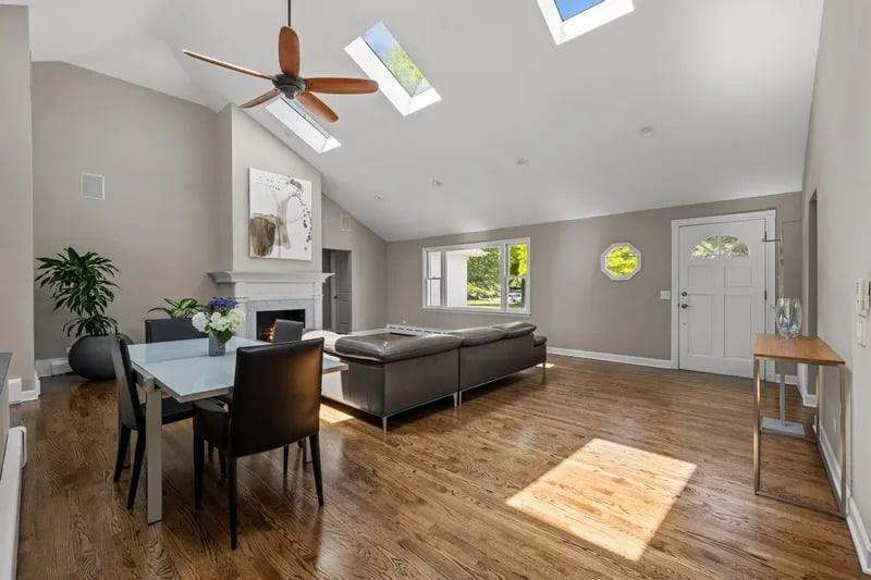 Open living and dining room with hardwood floors, vaulted ceiling, skylights, fireplace, and sectional sofa.