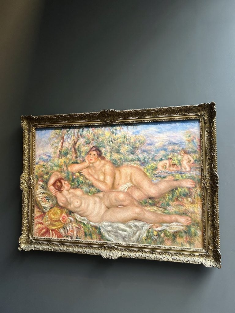 Ornate framed painting of reclining figures on a dark gray wall.